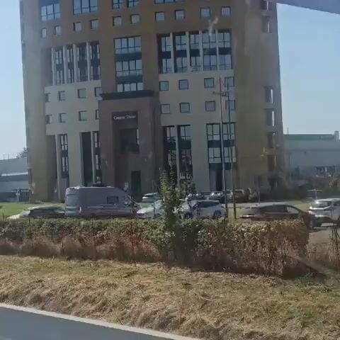 The video shows a building and a large inflatable ball on a grassy area outside. The ball is transparent and appears to have a person inside it. There are cars parked in front of the building. The video is shaky, suggesting it was filmed from a moving vehicle.