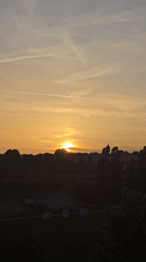 Sunset over urban silhouette with orange sky and contrails