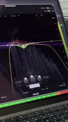 Here is a concise description of the video:

The video shows a close-up shot of a laptop screen displaying audio editing software, specifically FabFilter Pro-Q 3. The software interface shows a frequency spectrum with various equalizer bands adjusted. The person in the video is manipulating the EQ settings by turning knobs on the screen to adjust frequency and gain. The background includes some keyboard keys and a hint of surrounding environment.