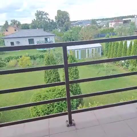 The video shows a panning view of a backyard with a fence, lawn, trees, and a greenhouse. A house is visible in the background. The sky is partly cloudy.