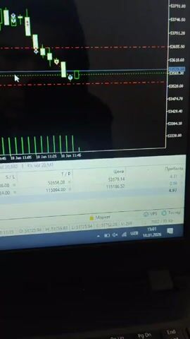 A close-up video shows a laptop screen displaying a stock trading platform. The platform shows a candlestick chart with green and red bars indicating price movements. Horizontal red and green lines mark support and resistance levels. Below the chart is a table with trading data, including prices, profit, and stop-loss/take-profit levels. The taskbar shows the date as January 18, 2026, and the time as 15:01. The laptop is black, and there is a reflection of the person filming on the screen.