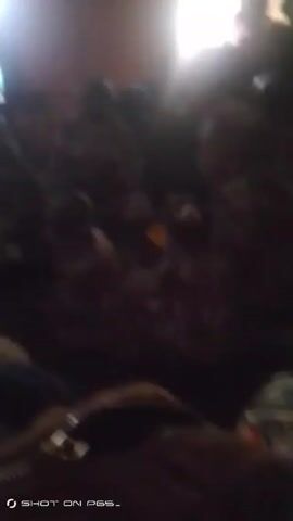 The video shows a dimly lit room packed with people. The light source seems to be coming from a window. The people are mostly obscured by shadow, but they appear to be sitting.  A bag is visible in the foreground.  The overall image quality is poor, with significant blur and darkness.