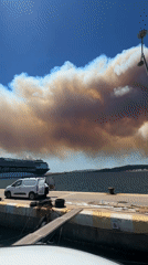 Smoke rises on Palamós pier with cruise ship docked nearby