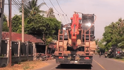Orange excavator transported by truck through Indonesian rural communities