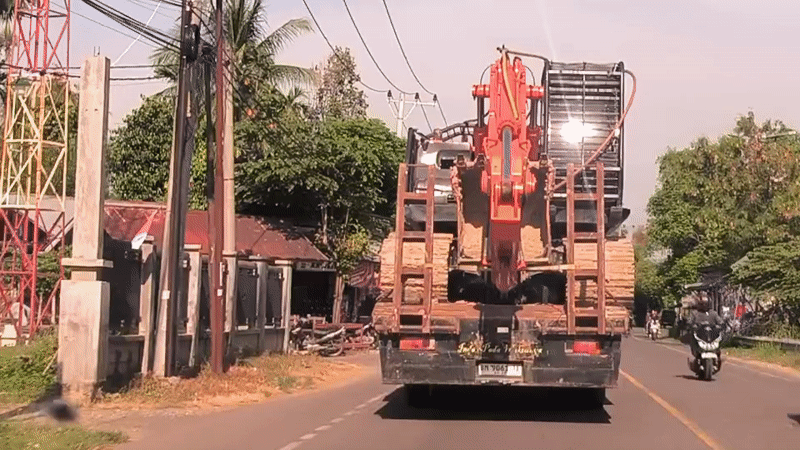 Orange excavator transported by truck through Indonesian rural communities