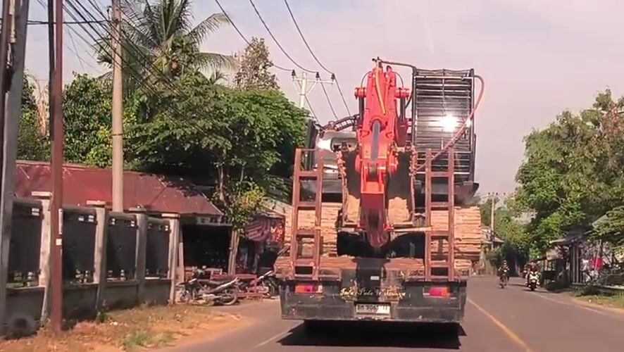 Orange excavator transported by truck through Indonesian rural communities