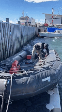 Person prepares inflatable boat at Ushuaia marina on clear day