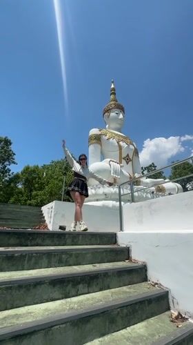 Woman descends temple stairs near Buddha statue in Thailand