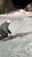 Snowboarder executes nighttime jumps on illuminated hill with rails