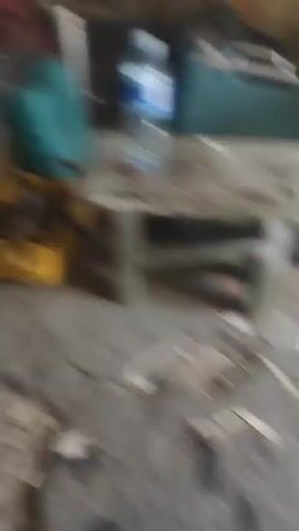 A light-colored dog is lying down on the ground. The dog is facing towards the right side of the frame. The dog's head is down and it appears to be resting or sleeping. The ground is rough and appears to be dirt or gravel. The lighting is dim and the focus is on the dog's face.