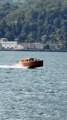 Red-hulled wooden boat speeds across a breezy Alpine lake