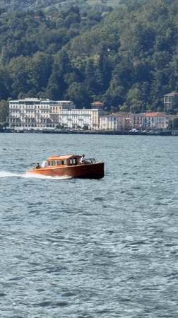 Red-hulled wooden boat speeds across a breezy Alpine lake