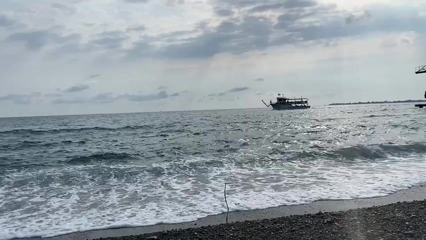 The video shows a boat on the ocean. The boat is white and has a canopy. There are many people on the boat. The water is choppy and there are waves. The sky is cloudy.