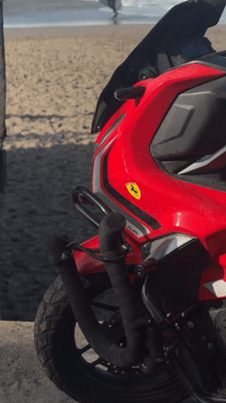 Man sits on motorcycle watching beach activity in Canggu
