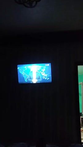 The video shows a television screen displaying content from the “KUN.UZ” website. The screen first shows a person standing in front of a world map, then transitions to an outdoor shot of a tall communications tower against a light blue sky. A bird flies near the top of the tower.