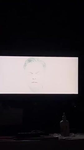 A screen displays a pale image of a man’s face with closed eyes, transitioning to an underwater scene with dark shapes and a glowing blue object. The screen is rectangular, set against a dark background, and there are blurred objects visible below it.
