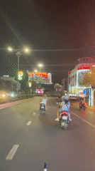 Three motorcyclists travel illuminated road near Lotte Mart Vietnam