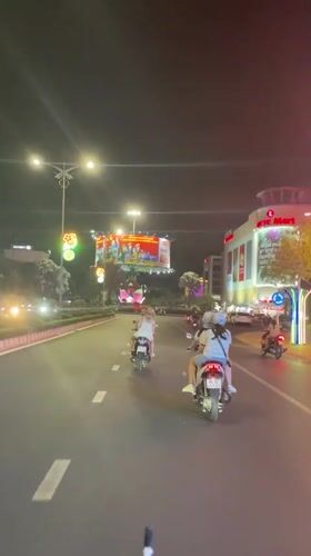 Three motorcyclists travel illuminated road near Lotte Mart Vietnam