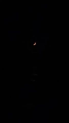 A crescent moon hangs in a black sky, reflected on the surface of dark water below.