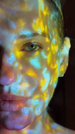 Person poses under colorful light projections during Dreiliņi sunset