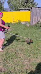 Woman trims grass with string trimmer in Markovo yard