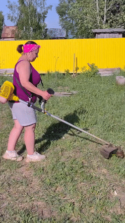 Woman trims grass with string trimmer in Markovo yard
