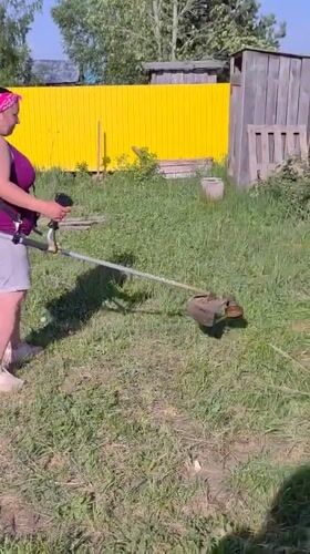 Woman trims grass with string trimmer in Markovo yard