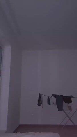 The video shows a close-up view of a window with a white handle, and a clothes drying rack with laundry on it. The room is dimly lit.