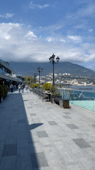 Pedestrians stroll Yalta's seaside promenade on partly cloudy day