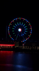 Colorful Ferris wheel observed during nighttime hours over waterfront