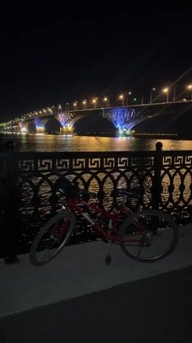 Red bike parked by Volga River near illuminated Saratov Bridge