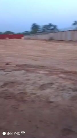 The video begins with a view of a large, dusty, dirt-covered lot with what appears to be red shipping containers in the background. There are also some trees in the distance. The camera then pans towards the side of a building where various metal pipes and cylinders are lying on the ground next to a burgundy cloth. There is an air conditioning unit outside the building. The camera moves inside briefly and then back outside, returning to the view of the lot with shipping containers and a covered structure in the distance. The quality of the video is somewhat grainy. At the bottom left corner of the screen is the text "itel P40 4G."