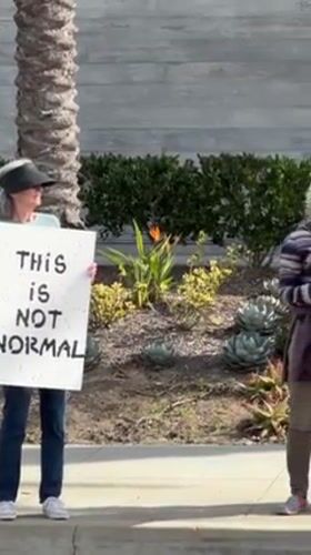Small protest group gathers with signs in Manhattan Beach