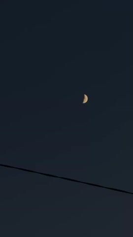 The video shows a crescent moon in a dark blue sky. A black electrical wire runs across the lower portion of the frame. A dog barks.