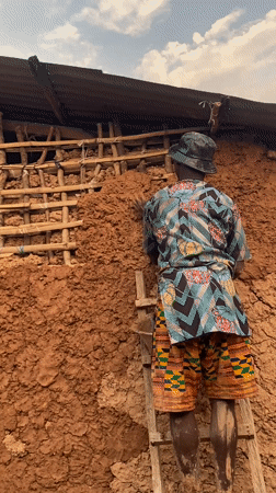 Man repairs mud house wall in Ufueseni, Nigeria