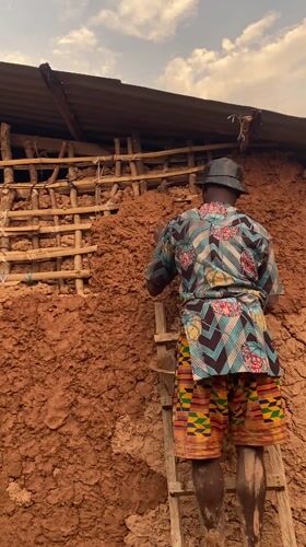 Man repairs mud house wall in Ufueseni, Nigeria
