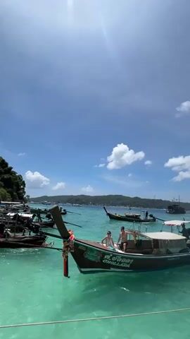 A group of people are on a boat on a sunny day. The water is clear and blue. There are other boats in the distance, and some islands.