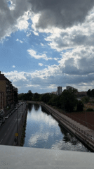 Cyclist rides along Milan canal under cloudy afternoon sky