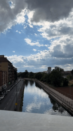 Cyclist rides along Milan canal under cloudy afternoon sky