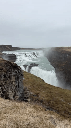 Tourists gather at Iceland's Gullfoss waterfall under cloudy skies