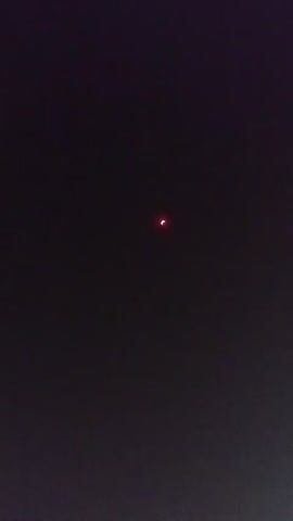 A very dark video shows a small, reddish-pink celestial object in the center of the frame, appearing as a sliver or crescent. The background is uniformly black, suggesting it is nighttime or deep space. There are no other discernible objects or features in the video.