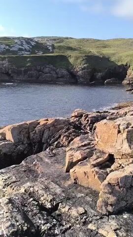 The video shows a rocky coastline with the ocean in the background. The rocks in the foreground are jagged and appear to be made of granite. The water is a deep blue and there are some small waves breaking on the shore. The sky is partly cloudy with some patches of blue visible. The overall impression is one of a wild and untamed natural landscape. The video is shot in landscape orientation and appears to be taken on a sunny day. There are no people or animals visible in the video.