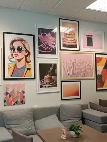 The media file shows a wall with several framed pictures hanging above a sofa and a table. The pictures feature a variety of subjects including pop art-style portraits, still life images of pancakes, abstract designs, and a floral motif. The overall aesthetic is modern and eclectic, with a focus on vibrant colors and graphic elements. 

The setting appears to be an indoor space, possibly a cafe or a lounge area, given the presence of comfortable seating and a table. The lighting suggests it is daytime, with artificial light from ceiling panels and natural light possibly coming from windows not visible in the frame. The wall is painted a neutral color, which allows the artwork to stand out.

Notable details include the different sizes and orientations of the frames, creating a dynamic arrangement on the wall. One picture shows a woman with blonde hair and sunglasses, rendered in a bold, graphic style. Another depicts a stack of pancakes, suggesting a culinary theme. There are also abstract geometric patterns and a close-up of a pink flower. 

No specific activity or event is depicted, but the comfortable seating suggests a space for relaxation or socializing. The overall mood is cheerful and visually stimulating, due to the colorful artwork. There is no visible text in the media file. The context provided indicates the location is Tallinn, Estonia, but this information is not visually evident from the media file itself.
