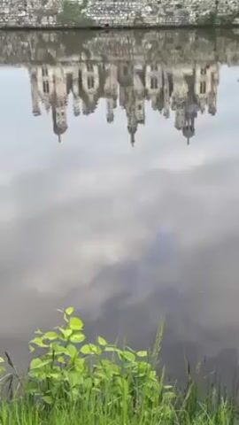 The video depicts a castle and its reflection in water. A stone barrier is visible at the top of the frame.  Vegetation grows near the water's edge at the bottom of the frame.