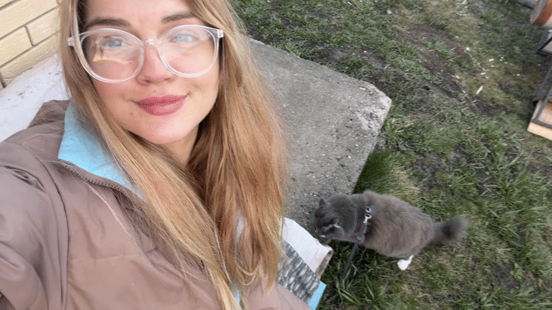 Woman films selfies with leashed cat in Russian village yard