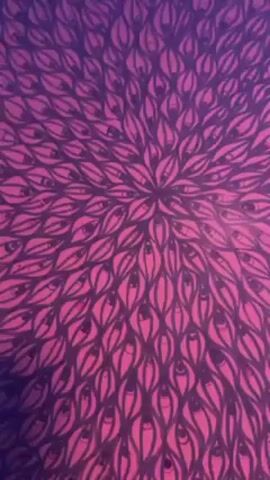 The video shows an artistic print, close up then further away. The artwork is composed of a multitude of shapes resembling eyes, arranged in a circular pattern emanating from the center. The colors transition from a deep purple to a vibrant pink. The artwork is framed and mounted on a wall. The lighting casts a purple hue over the room. The camera briefly pans to show a TV and another framed artwork. The room seems to be an entertainment or living area, enhanced with artistic decor. There is background music and faint conversation audible.