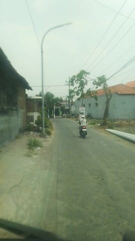 A motorcycle is seen riding on a street with buildings and trees on the side. The sky is overcast.