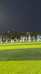 Dance group practices choreography on lit athletic field in Linghe