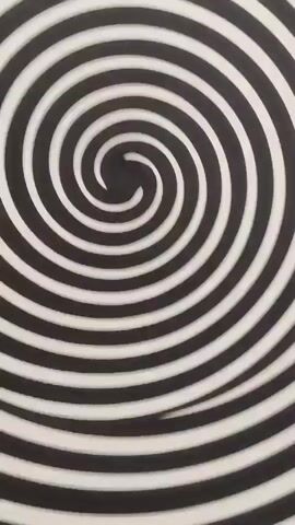 The video shows a close-up of a spinning vinyl record on a turntable. The record has a black and white spiral pattern that creates a hypnotic effect. The turntable is a silver Technics SL-1200. The video starts with a very close-up shot of the center of the record and slowly zooms out to reveal the entire turntable. The lighting is bright and even. The video is shot from a slightly high angle. There is no sound in the video.
