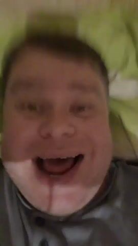 A man is lying on a bed with a green blanket. He looks directly at the camera with his mouth open, as if surprised, then smiles and says hello. He then raises his hand to his forehead as if to salute, and then waves. He says "Let's go" and smiles broadly at the camera.